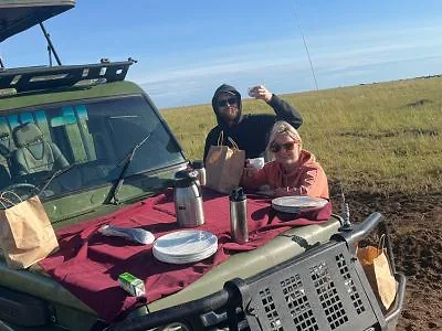 Kaksi henkilöä syö aamiaista safariautossa