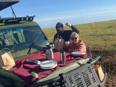 Kaksi henkilöä syö aamiaista safariautossa